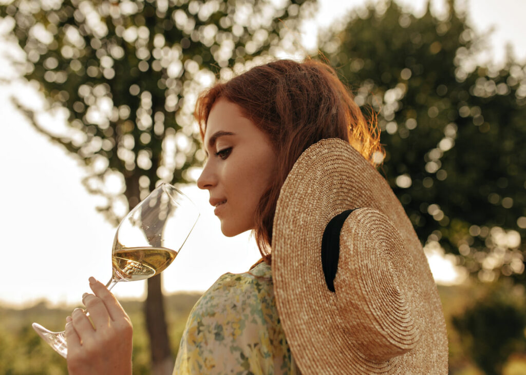 mujer-joven-con-sombrero-de-paja-bebiendo-una-copa-de-vino-al-aire-libre