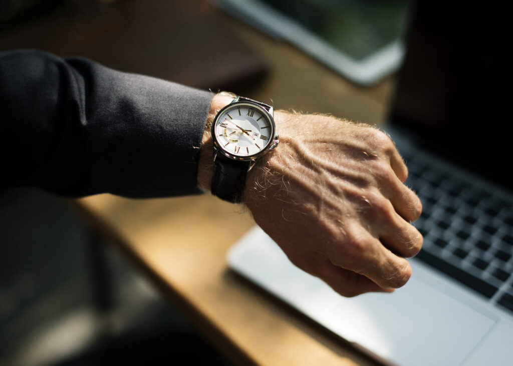 muñeca-de-un-hombre-que-lleva-un-reloj-con-un-ordenador-de-fondo