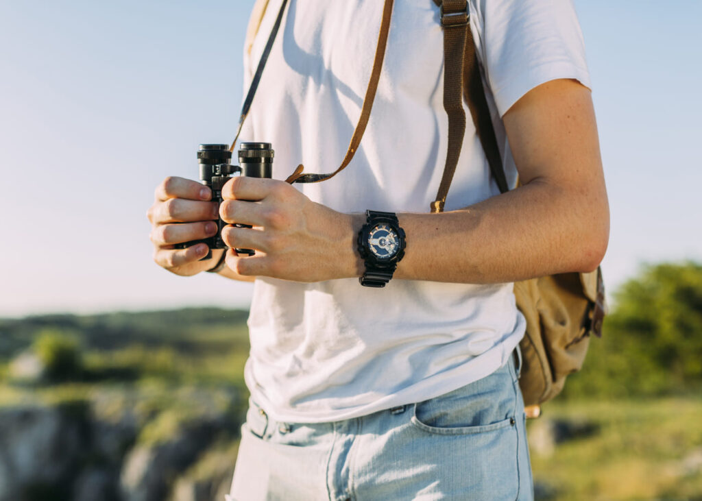 primer-plano-de-hombre-que-sostiene-prismáticos-con-un-reloj-en-la-muñeca-en-plena-naturaleza