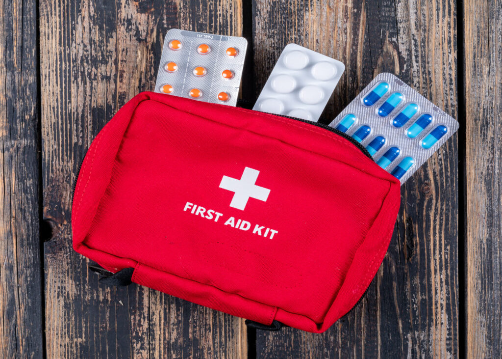 botiquin-de-primeros-auxilios-rojo-con-blister-de-medicamentos-que-sobresale-sobre-una-mesa-de-madera