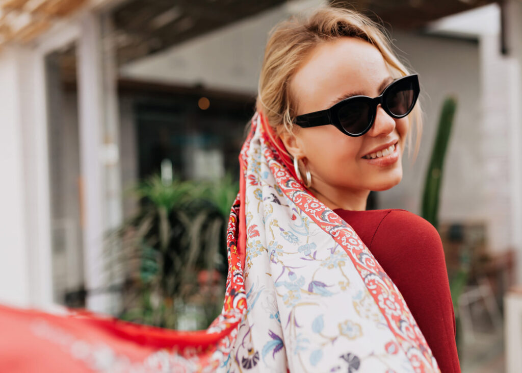 mujer-de-perfil-que-sonrie-con-gafas-de-sol-y-un-largo-panuelo-rojo-en-el-cabello
