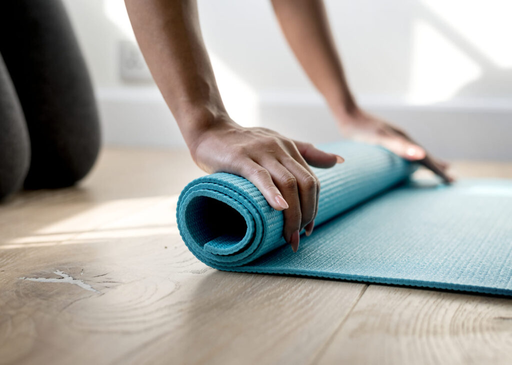 mujer-de-rodillas-que-enrolla-su-esterilla-de-yoga