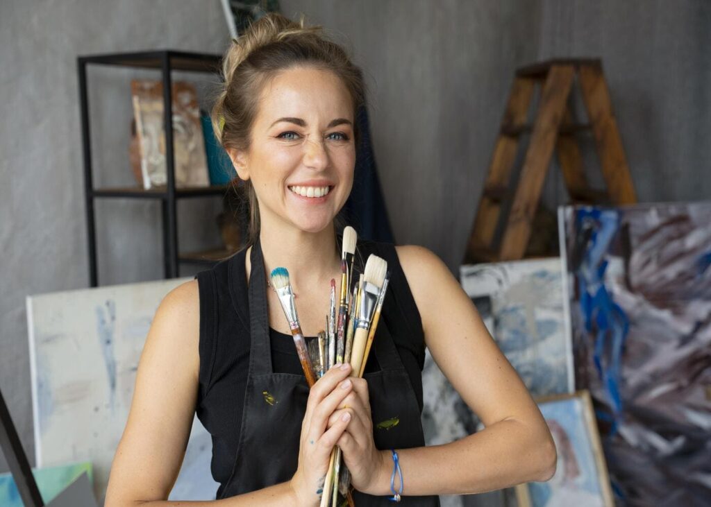 mujer-pintora-que-sonrie-sosteniendo-pinceles-en-las-manos