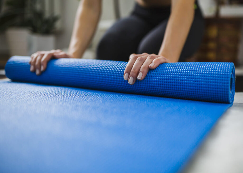 mujer-que-enrolla-una-esterilla-de-gimnasia-azul-en-el-suelo