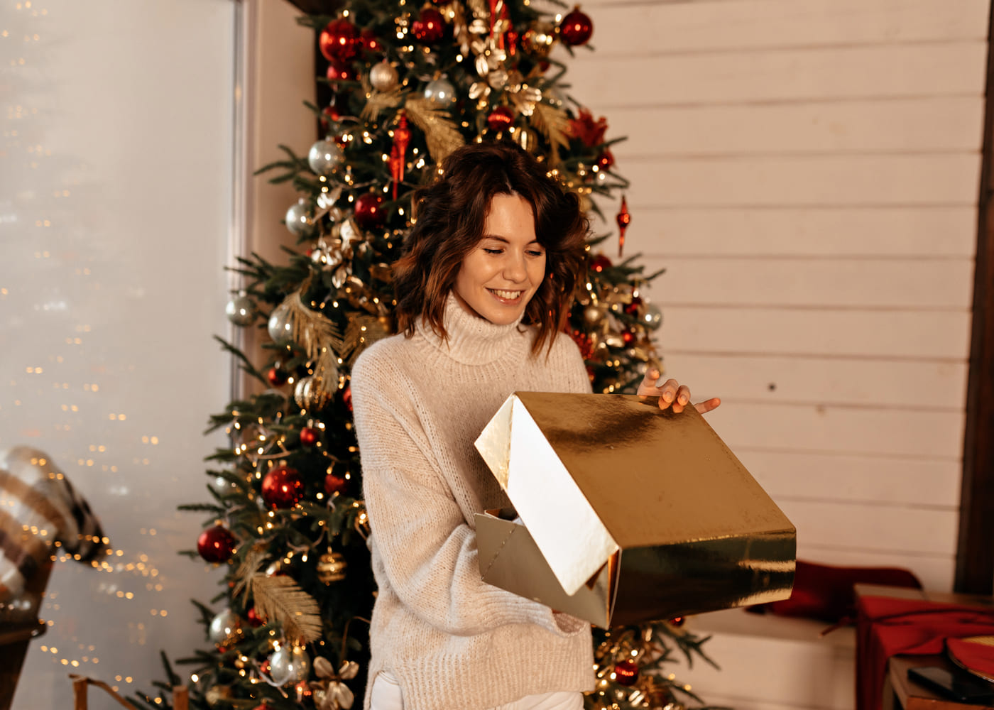 mujer-que-sonrie-al-abrir-su-regalo-de-navidad-delante-del-arbol-de-navidad