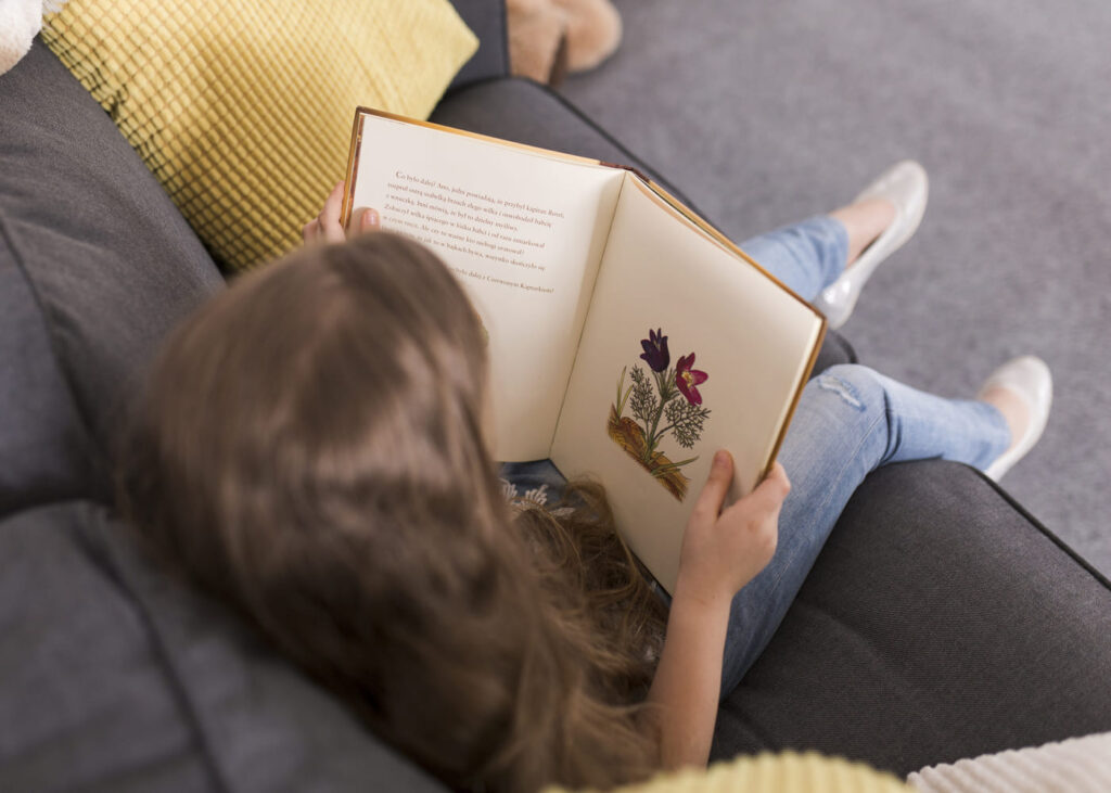 niña-pequeña-que-lee-un-libro-infantil-sentada-en-el-sofá