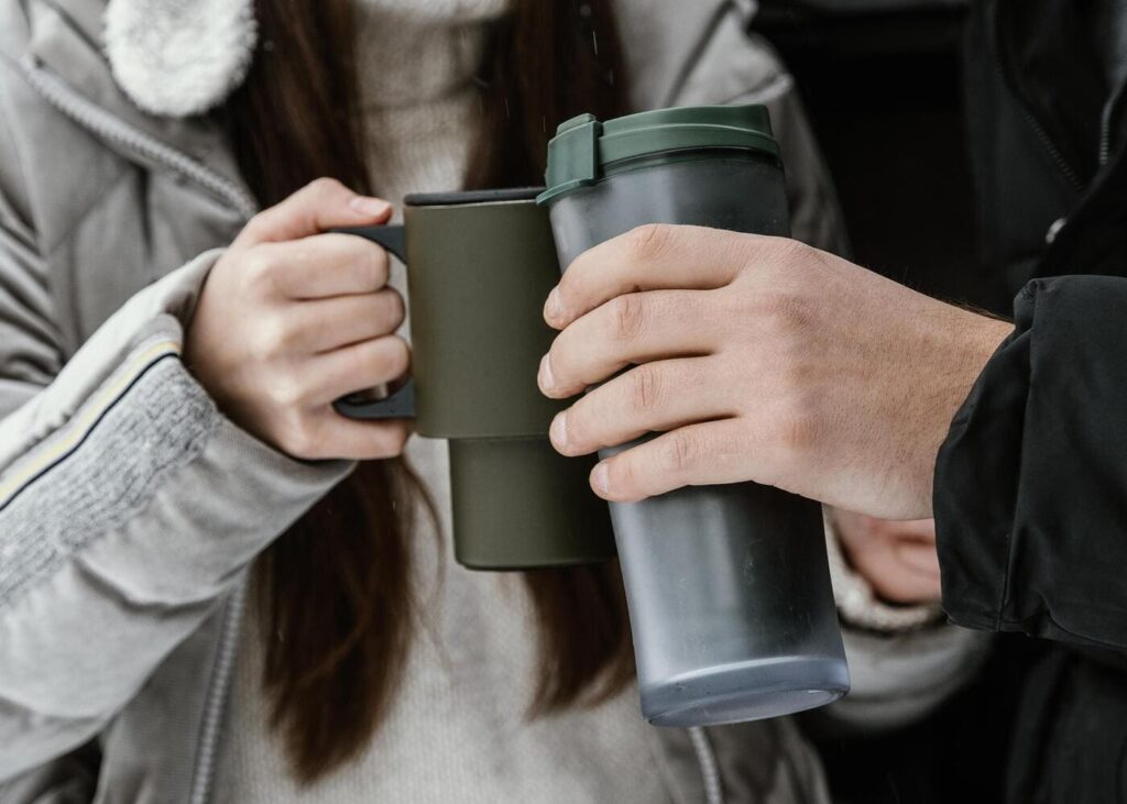 primer-plano-de-dos-personas-sujetando-cada-una-un-mug-isotermico