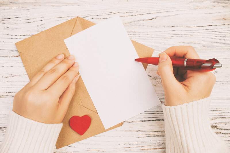 primer-plano-de-manos-de-una-mujer-con-una-carta-blanca-y-un-sobre-marron-con-un-corazon-rojo