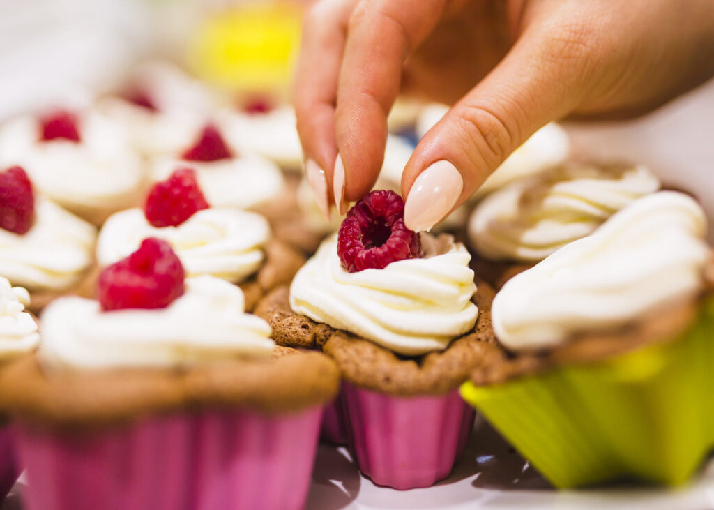 primer-plano-de-una-mano-de-mujer-que-pone-una-frambuesa-sobre-un-cupcake