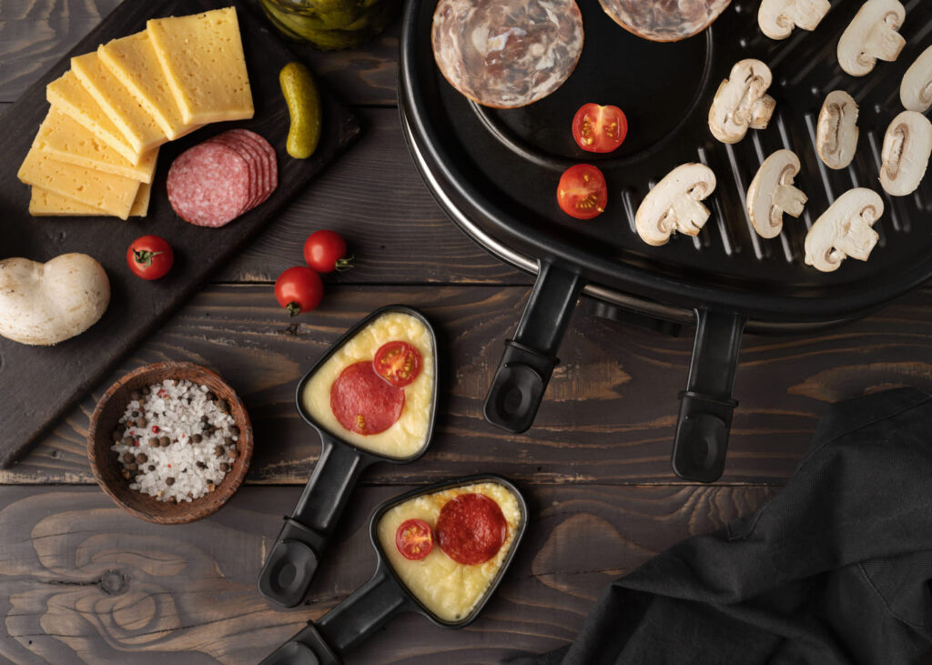 vista-desde-arriba-de-un-aparato-de-raclette-con-ingredientes-en-la-mesa