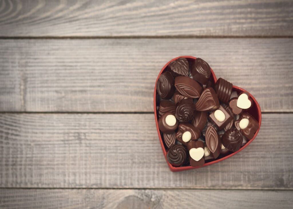 caja-de-corazon-roja-llena-de-chocolates-sobre-un-fondo-de-madera-gris